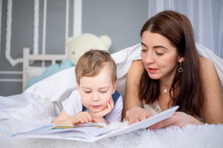 Mom Reads A Book To The Child Or Teaches Him At Home On The Bed Happy